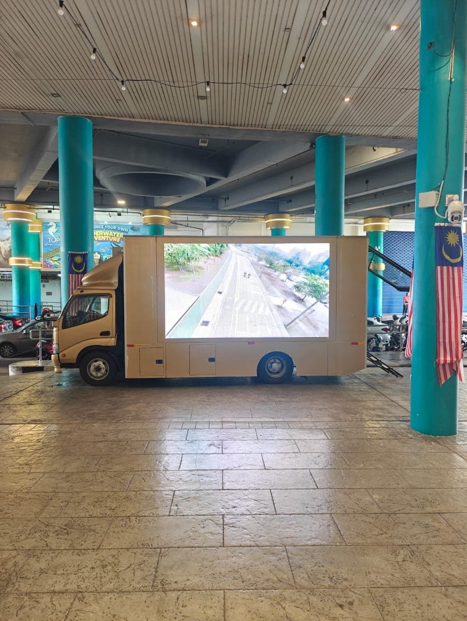 LED truck parked in a covered plaza, its screen playing a road video