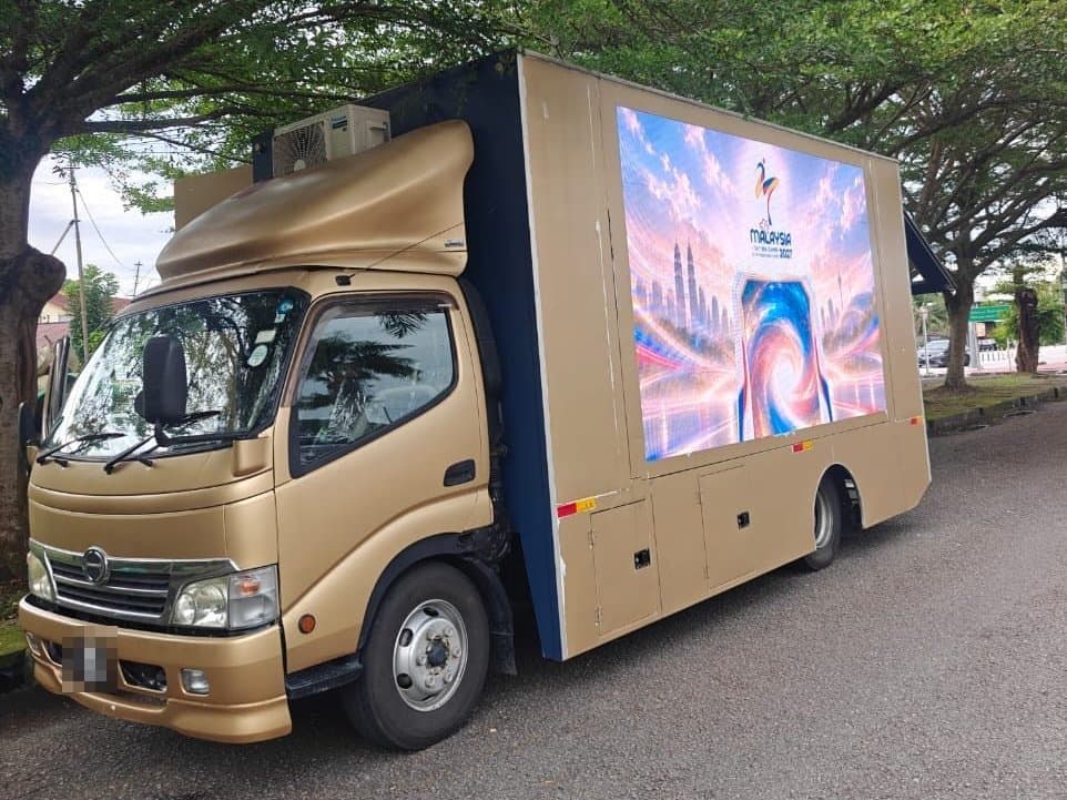 LED truck showing a 2027 Malaysia SEA Games graphic, parked under trees in Penang